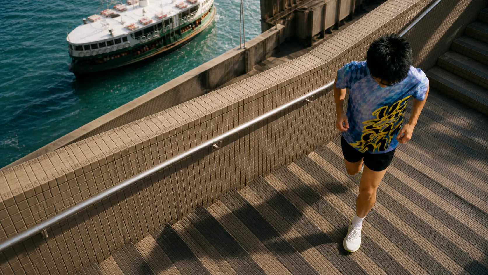 Runner descending tiled Hong Kong harbour stairs in a Wazup tee